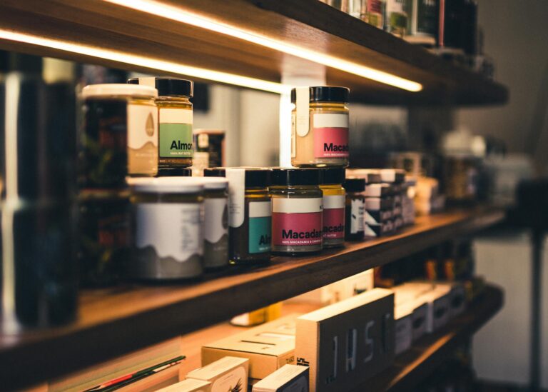 Close-up of artisan almond and macadamia nut butter jars on a wooden shelf in a shop.